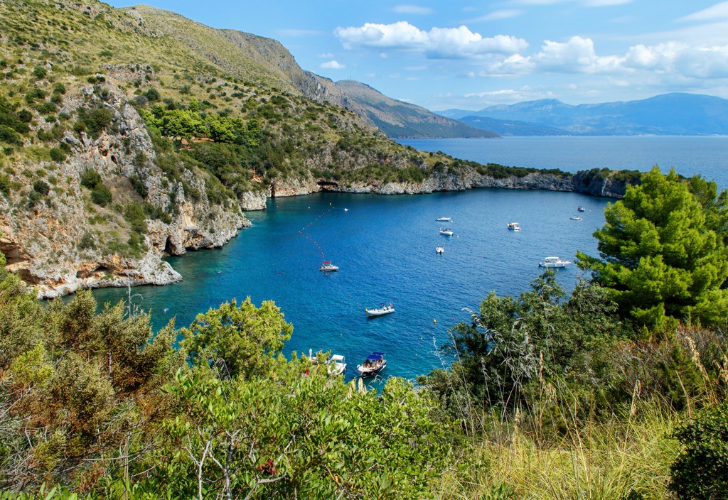 Baai aan de Amalfikust met rotsen, groen en bootjes op helderblauw water in Zuid-Italië.