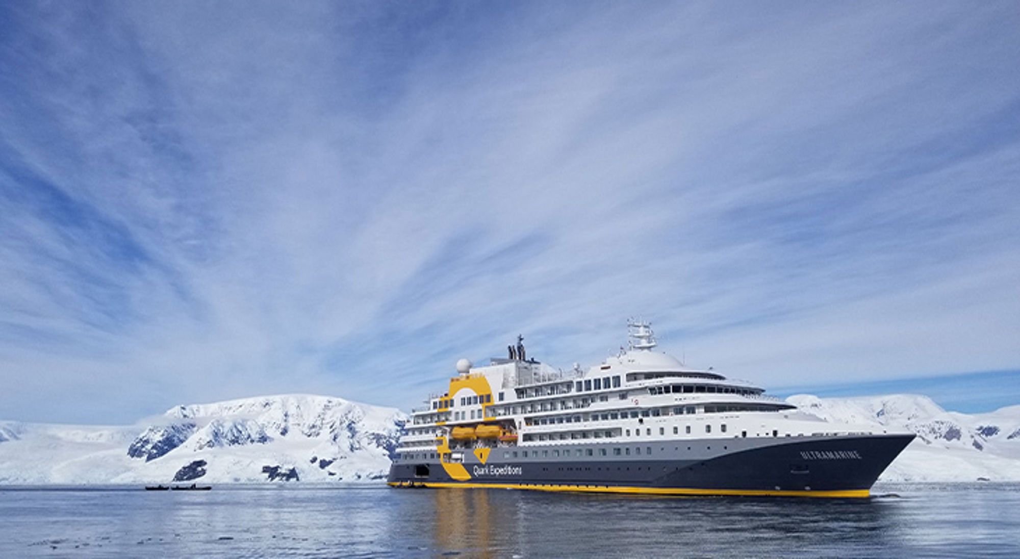 Ultramarine Expeditieschip op zee bij besneeuwde bergen onder een heldere lucht.