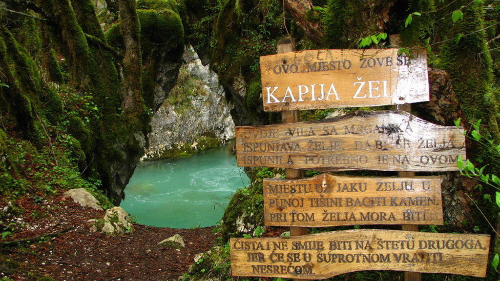Houten wegwijzer bij een turquoise bron in een boskloof tijdens de Groepsrondreis Balkan.