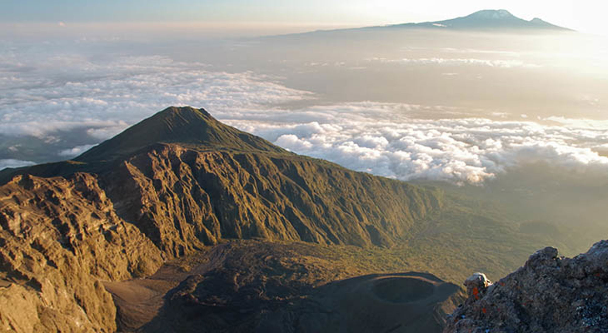 Uitzicht vanaf de Kilimanjaro over de vulkanische bergkam en een zee van wolken bij zonsopgang.