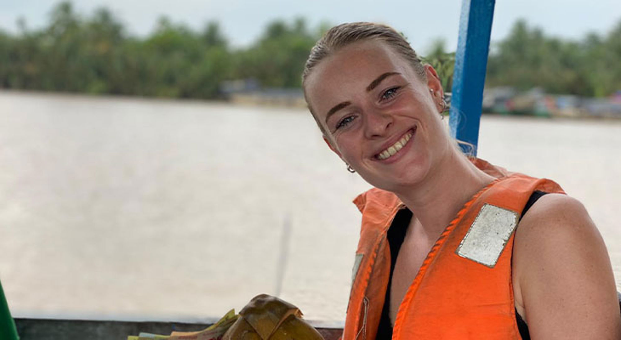 Lisa Lommerse Vrouw met reddingsvest glimlacht op een boot, met rivier en groene oever op de achtergrond.