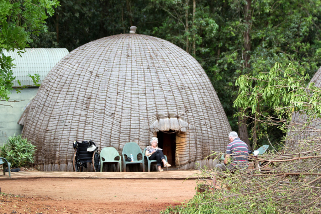 Ronde rieten hut in Zuid-Afrika met reizigers bij de ingang tijdens een groepsrondreis kampeerreis.