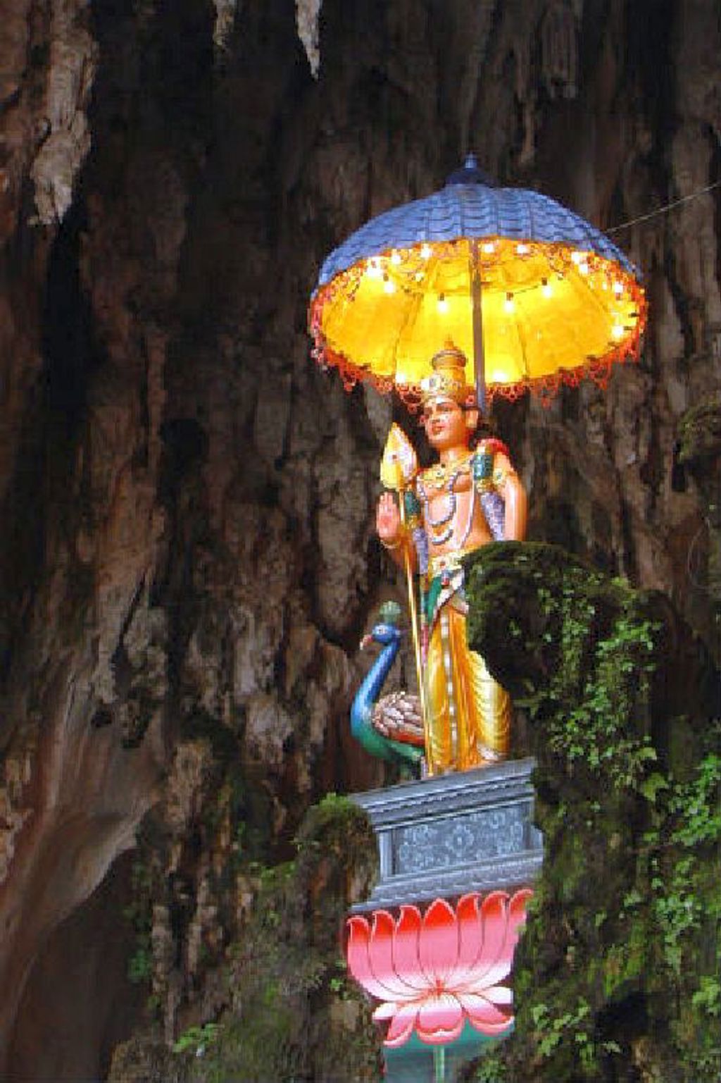 Standbeeld bij de Batu Caves, Maleisië, verlicht onder een parasol in een grot.