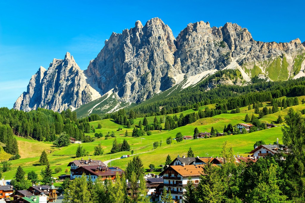Groene alpenweiden en bergdorp met rotsmassief in de Dolomieten, Italië.