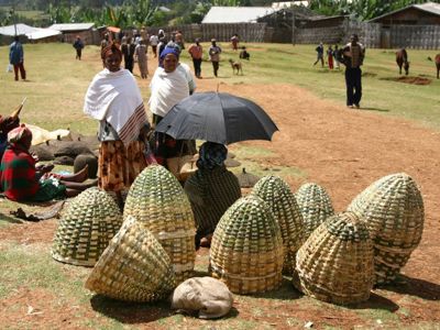 Markt in Ethiopië met gevlochten manden en vrouwen in traditionele kleding langs een zandpad.