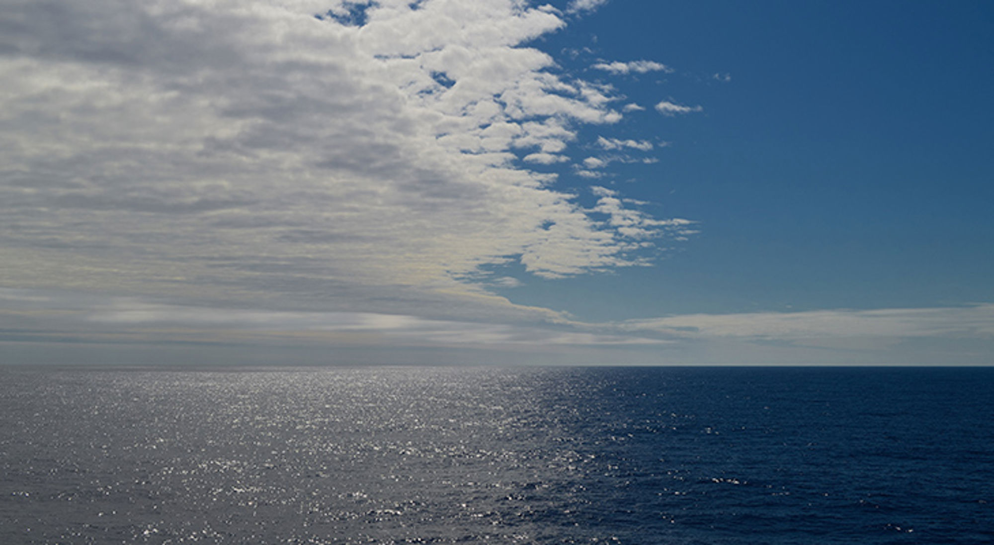 drake-passage Uitzicht over de open zee met glinsterend water en wolkenlucht aan de horizon.