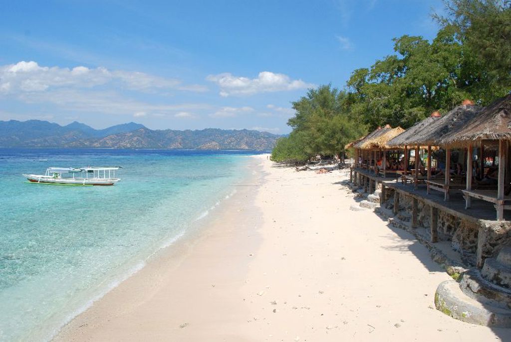 Wit zandstrand met azuurblauwe zee, bootje en strandhutten op Lombok tijdens groepsrondreis Java, Bali en Lombok.