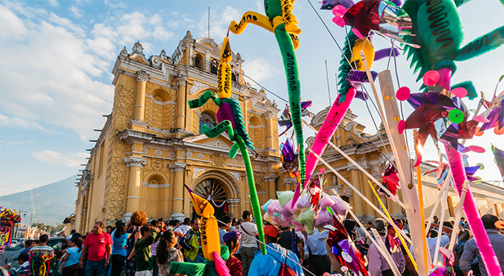 Kleurrijke festiviteit met vliegers en feestgangers voor de gele kathedraal in Antigua Guatemala.