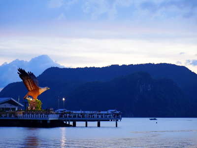 Adelaarsbeeld op de pier van Langkawi bij zonsondergang, met bergen op de achtergrond.