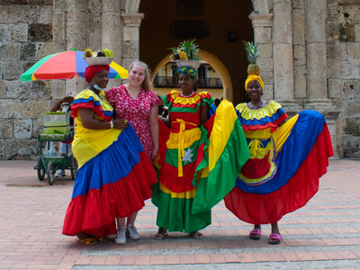 Vrouwen in kleurrijke jurken poseren met fruit op het hoofd bij de stadsmuur van Cartagena, Colombia.