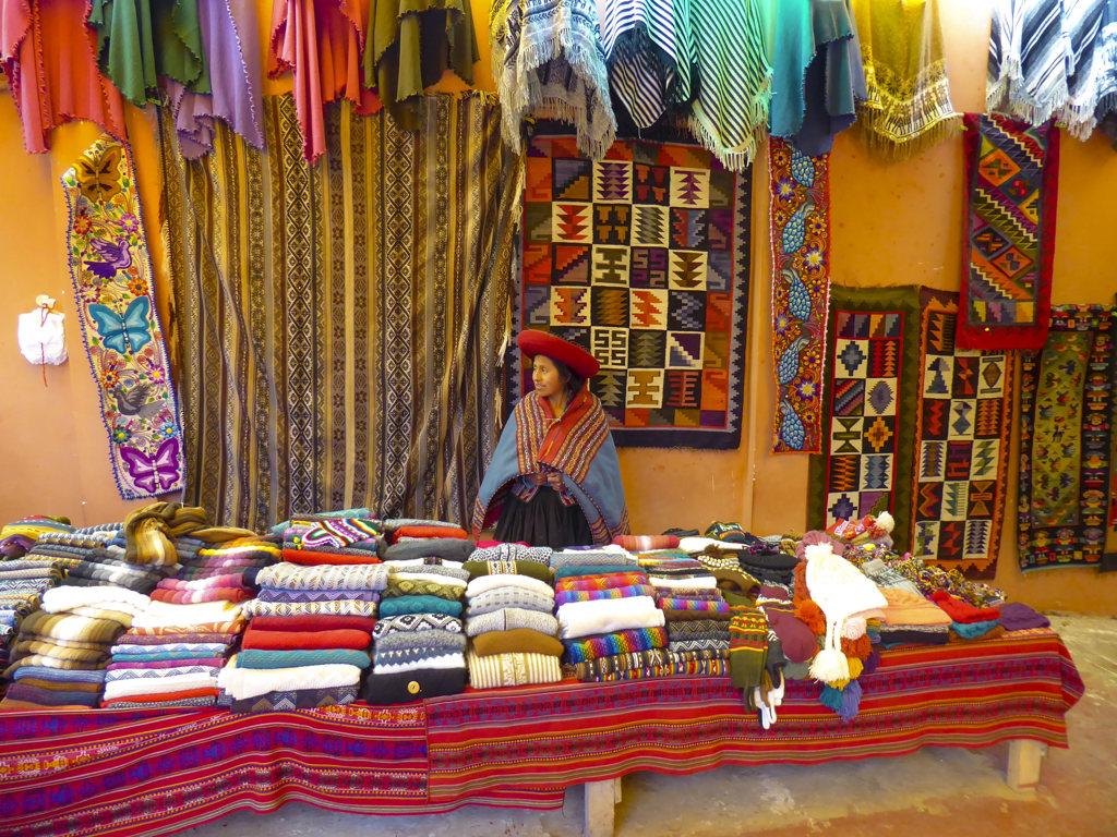 Vrouw bij kleurrijke textielkraam op markt in Peru tijdens rondreis.