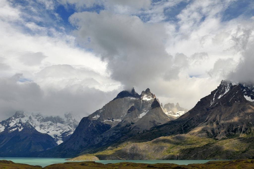 Berglandschap in Patagonië, Argentinië, met besneeuwde pieken, wolken en een turkoois meer.