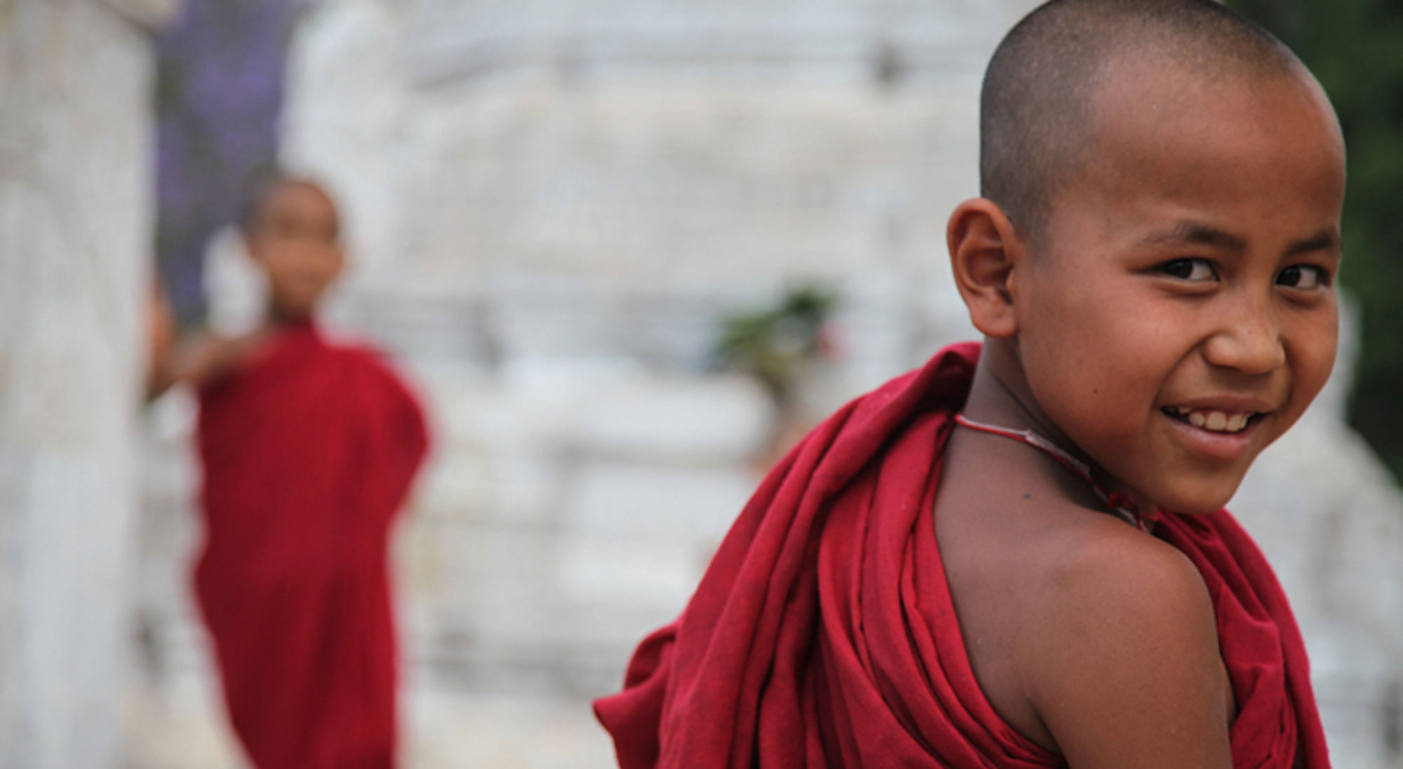 Jonge monnik in Myanmar Glimlachende jonge monnik in rode gewaden met een tweede monnik onscherp op de achtergrond.