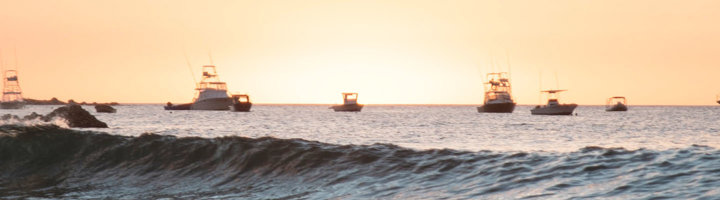 Zonsondergang bij Tamarindo met golven op zee en boten aan de horizon.