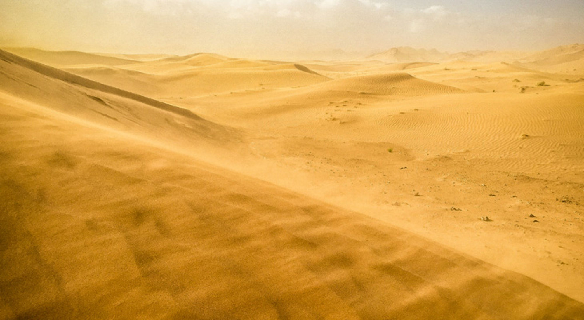 Uitgestrekte zandduinen in een woestijnlandschap met opwaaiend zand.