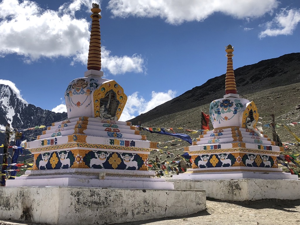 Boeddhistische stupa’s met gebedsvlaggen in Ladakh, India, tegen een berglandschap en blauwe lucht.