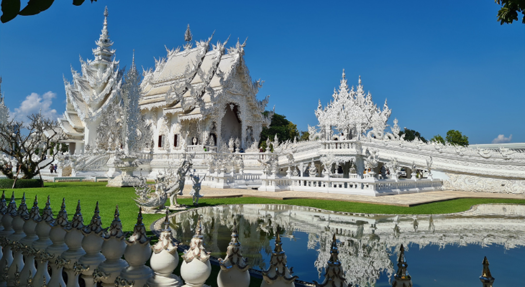 Chiang Rai White Temple Witte tempel Wat Rong Khun in Chiang Rai met weerspiegeling in de vijver onder blauwe lucht.