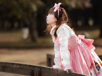 Jonge vrouw in roze lolita-outfit leunt op een houten hek in een park in Japan.