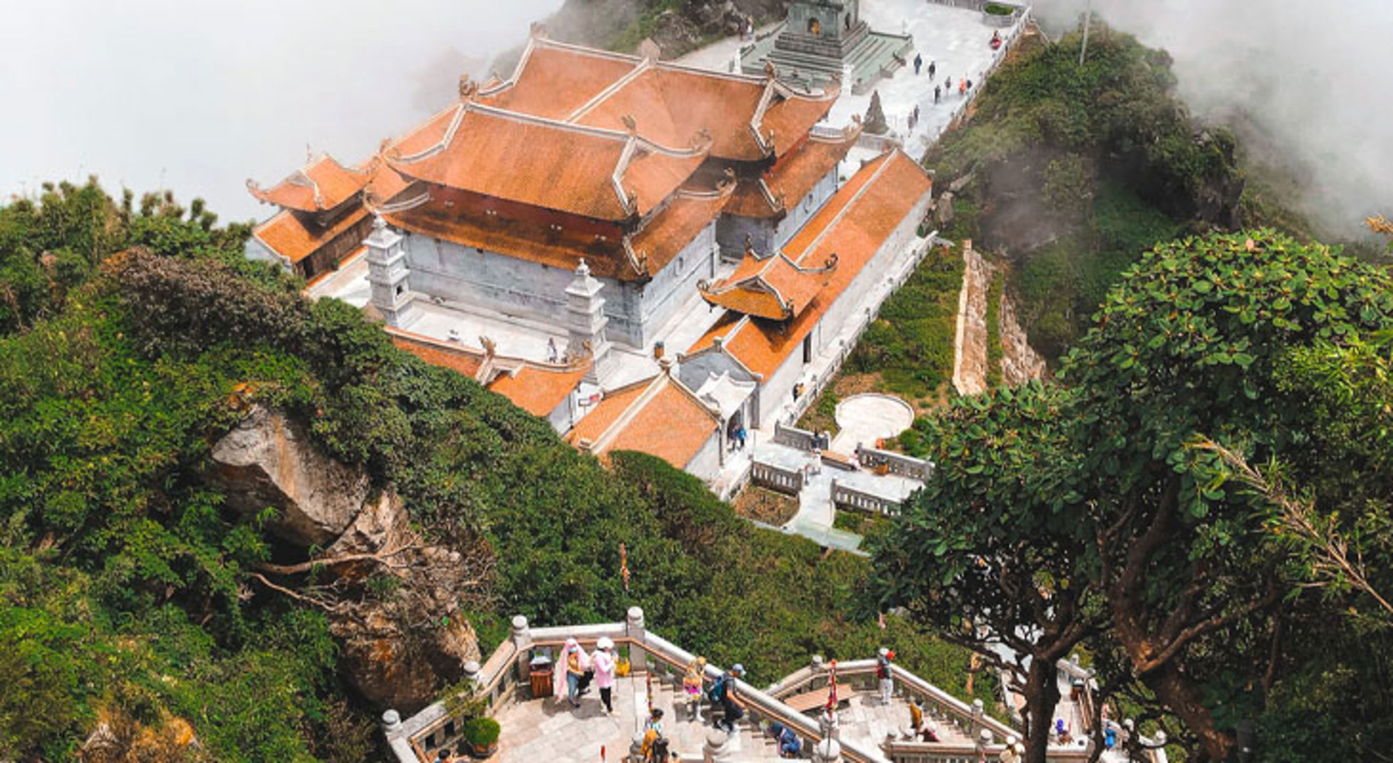Fansipan Bergtempel met oranje daken tussen groene rotsen in Vietnam, gezien vanaf een uitkijkpunt.