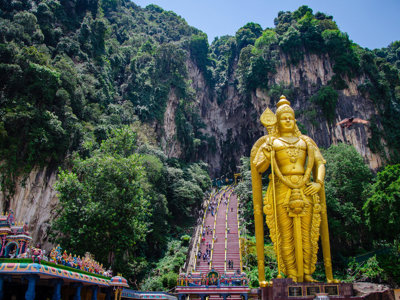 Gouden Murugan-beeld bij de Batu Caves met kleurrijke trappen en kalksteenrotsen in Maleisië.