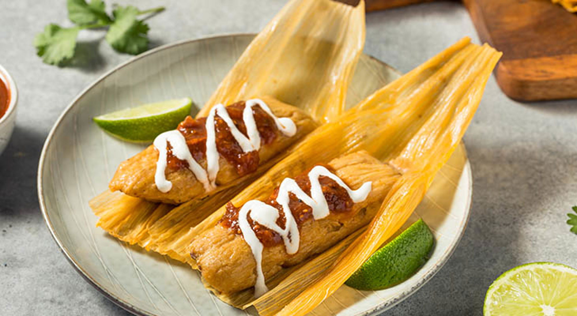 Keuken Belize Tamales in maïskolfblad met salsa, zure room en limoenpartjes op een bord.