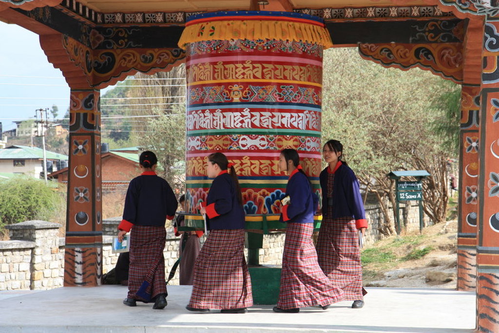 Bhutanese vrouwen lopen rond een kleurrijke gebedsmolen bij een tempel, tijdens groepsrondreis Sikkim en Bhutan.