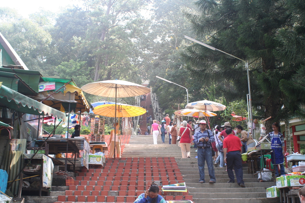 Drukke trap naar Doi Suthep-tempel in Chiang Mai met marktkraampjes en parasols.