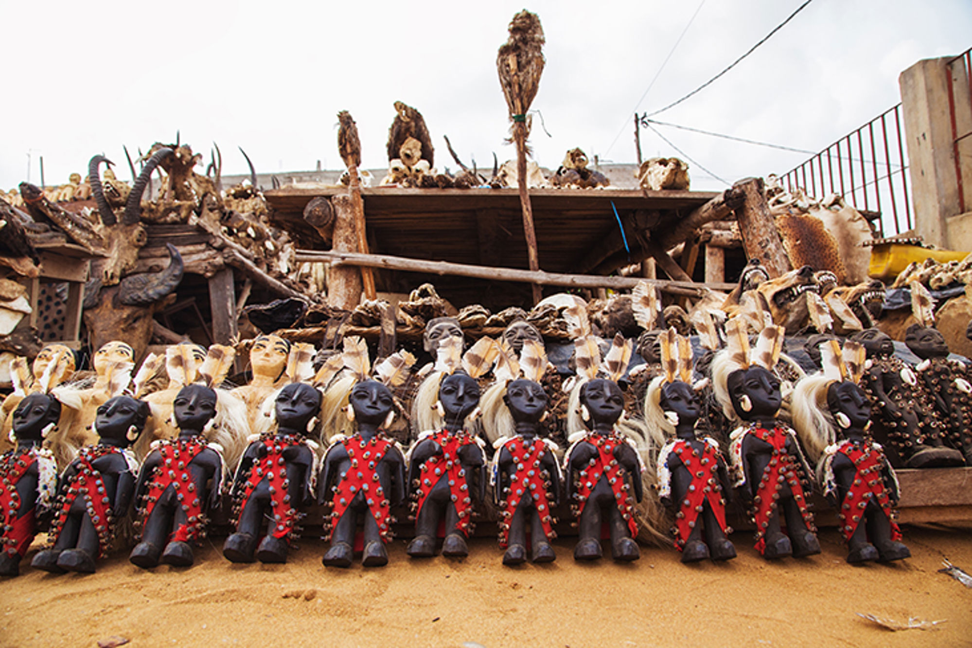 voodoo beeltjes in benin Rij traditionele poppen met kralen en schelpen op een markt, met dierenschedels en huiden op de achtergrond.