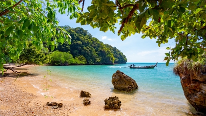 Tropisch strand in Thailand met turquoise zee, rotsen en een longtailboot voor de kust.
