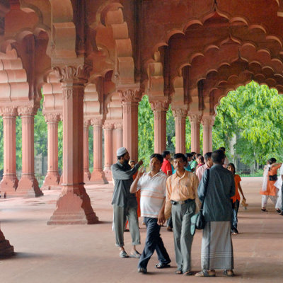 Bezoekers in een zuilengalerij met roodstenen bogen bij een historisch monument in Noord-India.