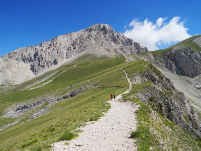 Wandelpad over een bergkam in de Centrale Apennijnen met wandelaars en een rotsachtige bergtop op de achtergrond.