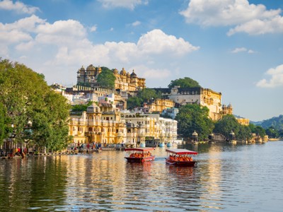 Stadsgezicht van Udaipur aan Lake Pichola met paleizen op de heuvel en boten op het water.