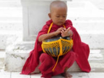 Jonge monnik in rode gewaden met aalmoesschaal bij een tempel in Myanmar.