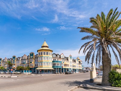 Historische gebouwen aan de boulevard in Swakopmund, Namibië, met palmbomen onder een blauwe lucht.