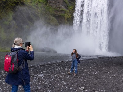 Reizigers bij de Skógafoss-waterval op IJsland, waar een vrouw een foto maakt van haar reisgenoot.