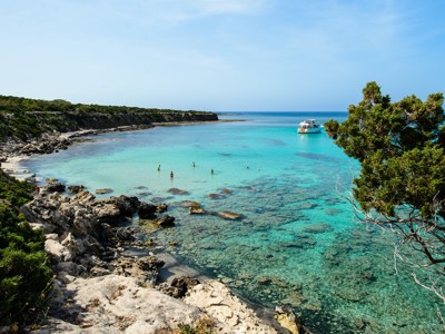 Turquoise baai met rotsachtige kust en boot voor de kust van Cyprus tijdens een familiereis.