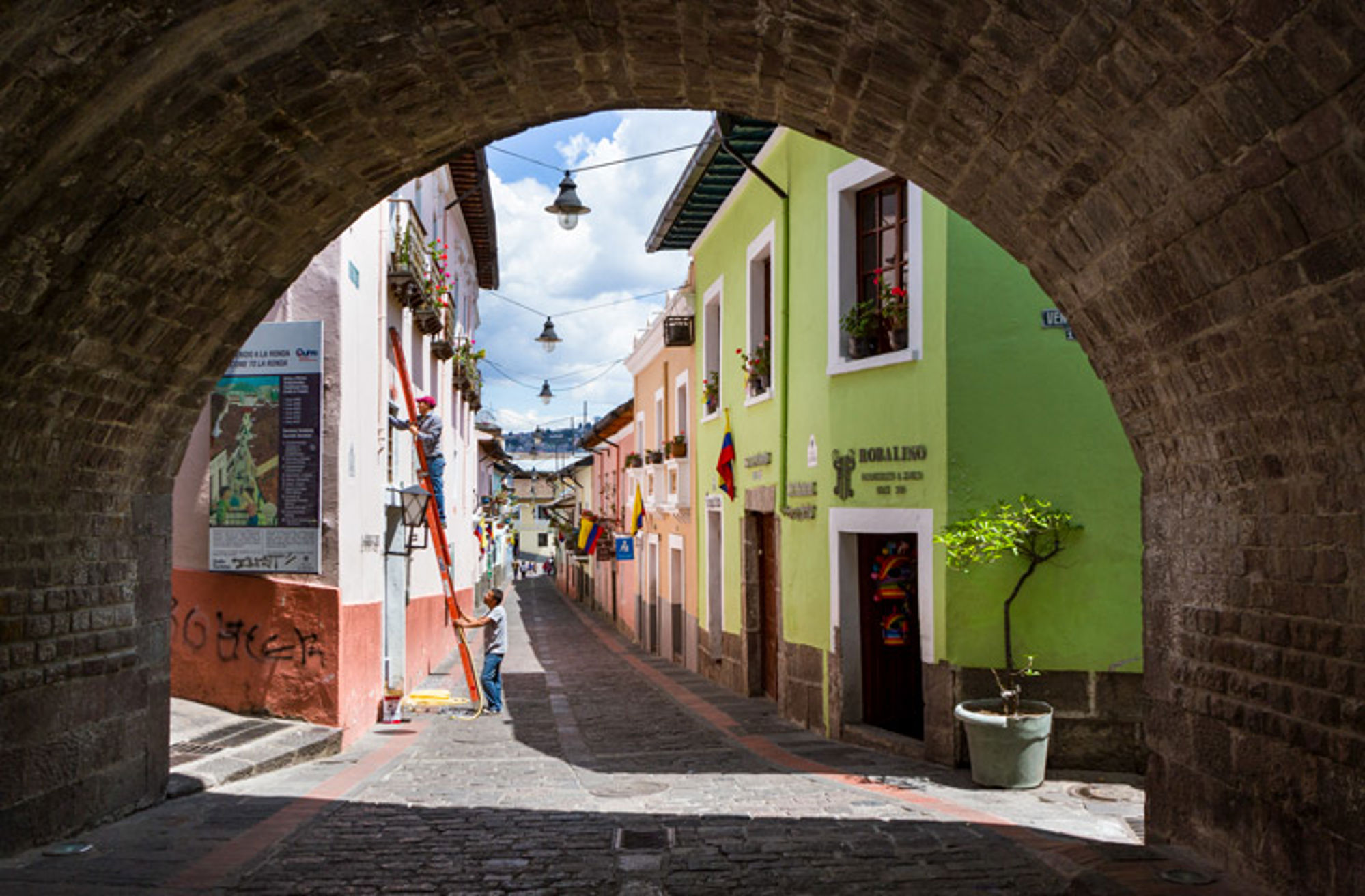 Ecuador onderdoorgang en straat Straat in Quito met kleurrijke koloniale gevels, Ecuadoriaanse vlaggen en een stenen boog op de voorgrond.