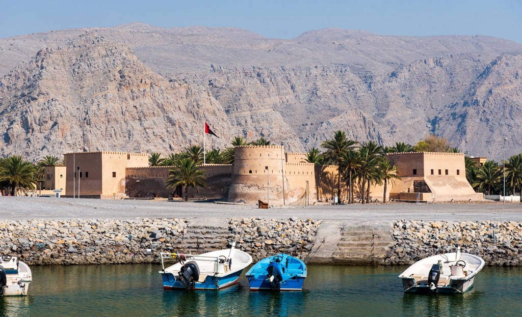 Omaans fort aan de kust met palmbomen en vissersboten, met bergen op de achtergrond tijdens groepsrondreis Oman en Dubai.
