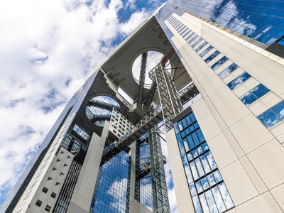 Umeda Sky Building in Osaka met futuristische brug en open ronde top tegen een blauwe lucht.