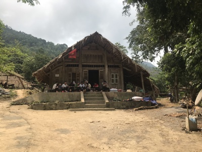 Traditioneel houten huis met rieten dak in de bergen van Vietnam, met bewoners op de veranda.