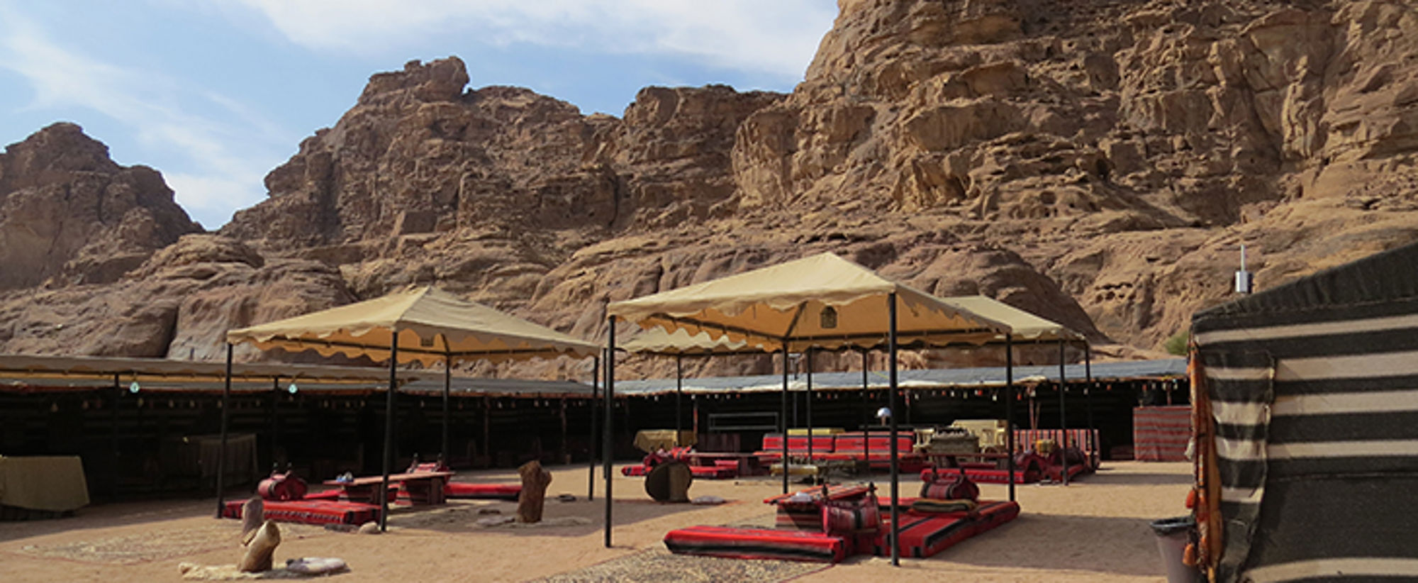 Bedoeïentent in Jordanië Bedoeïenenkamp met zitkussens en schaduwdoeken in de woestijn, met rotsgebergte op de achtergrond.