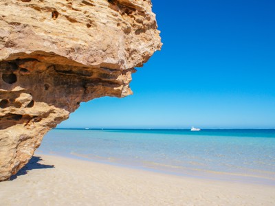 Kalkstenen rotsformatie aan een wit zandstrand met helderblauw zeewater in West-Australië.