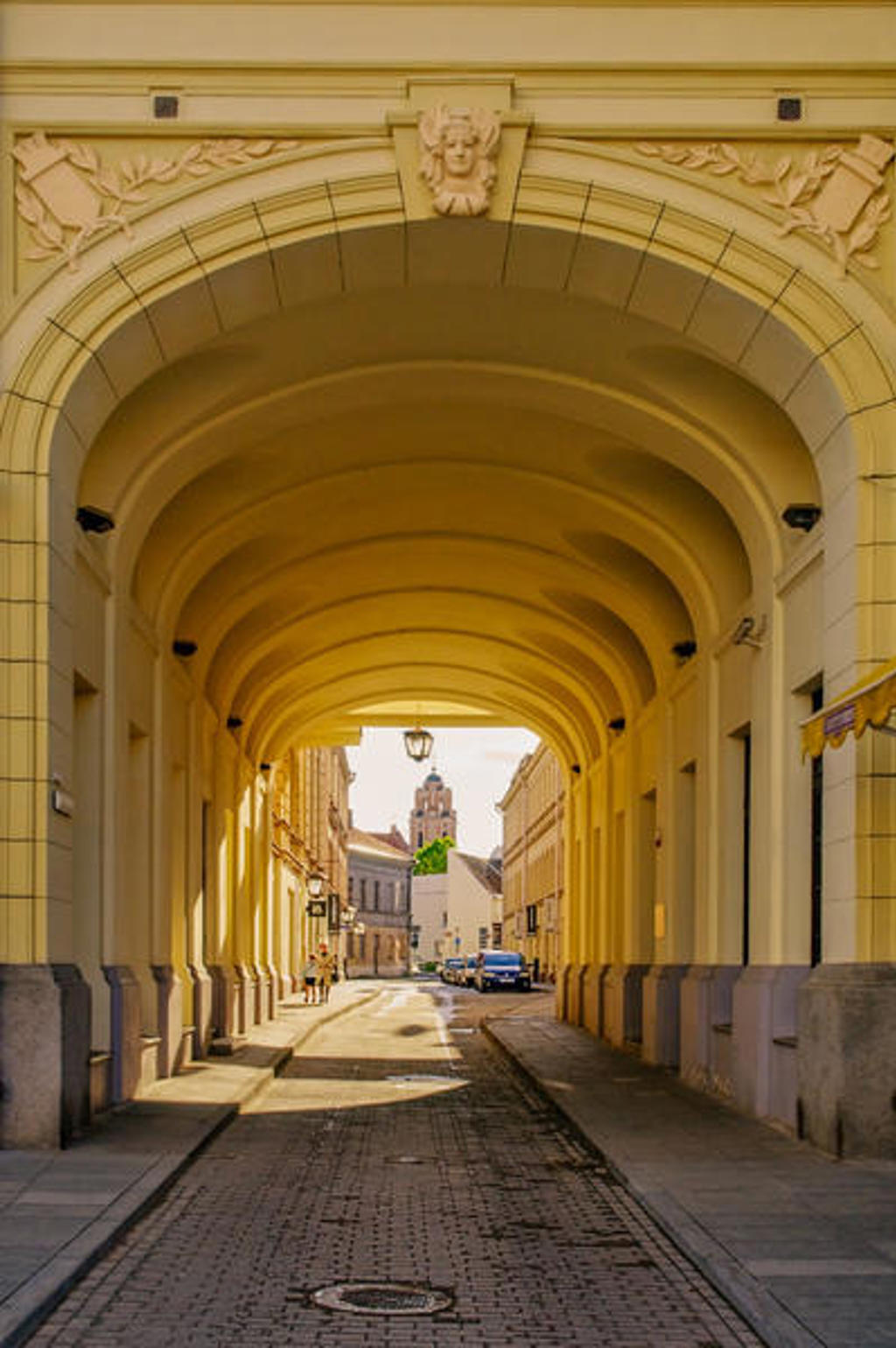 Doorkijk door een historische poortgang naar een straat in Vilnius, tijdens de familiereis Polen en Baltische Staten.