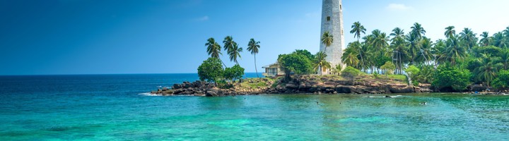 Witte vuurtoren bij Galle aan de kust van Sri Lanka, met palmbomen en helderblauwe zee.