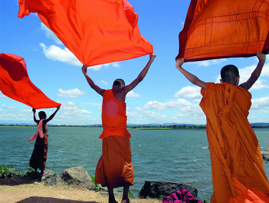 Boeddhistische monniken houden oranje doeken omhoog aan een meer in Sri Lanka.