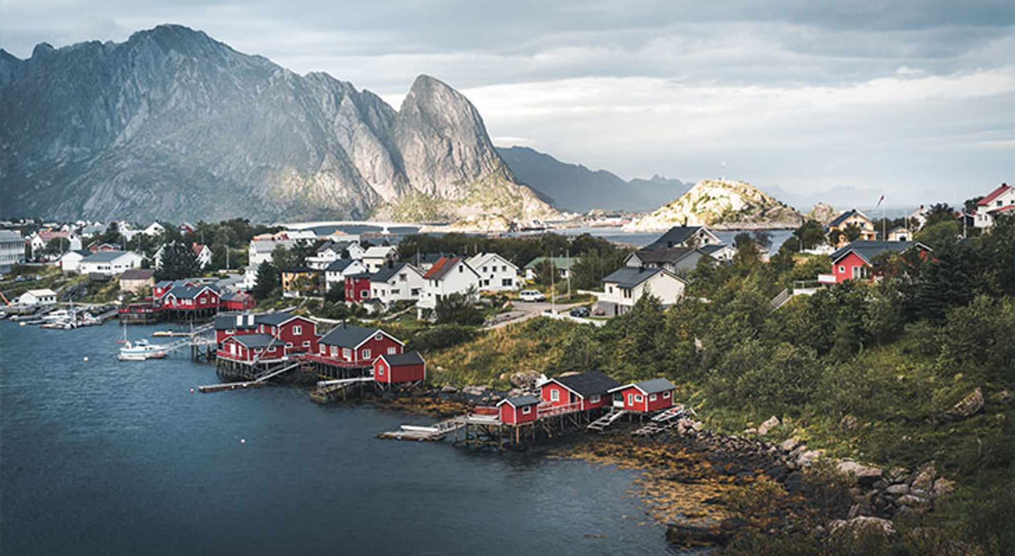 Lofoten Noorwegen Rode vissershuisjes aan de kust met bergen op de achtergrond in Lofoten, Noorwegen.