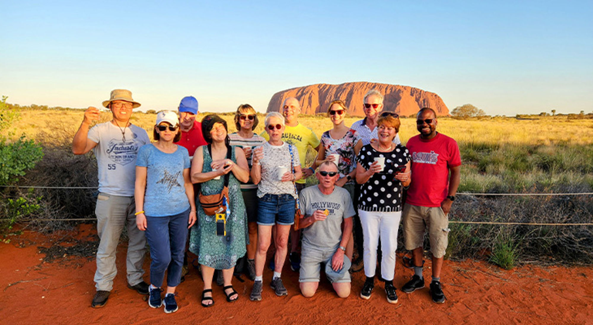 Groepsfoto van reizigers bij Uluru (Ayers Rock) in Australië tijdens zonsondergang.
