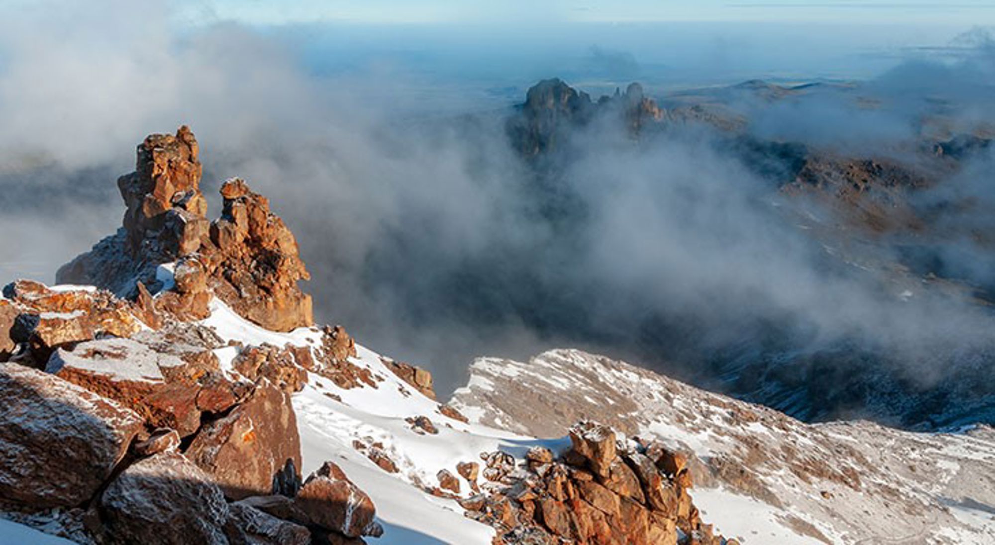 mount-kenya Besneeuwde rotsen en bergtoppen boven de wolken, met mist in een uitgestrekt berglandschap.