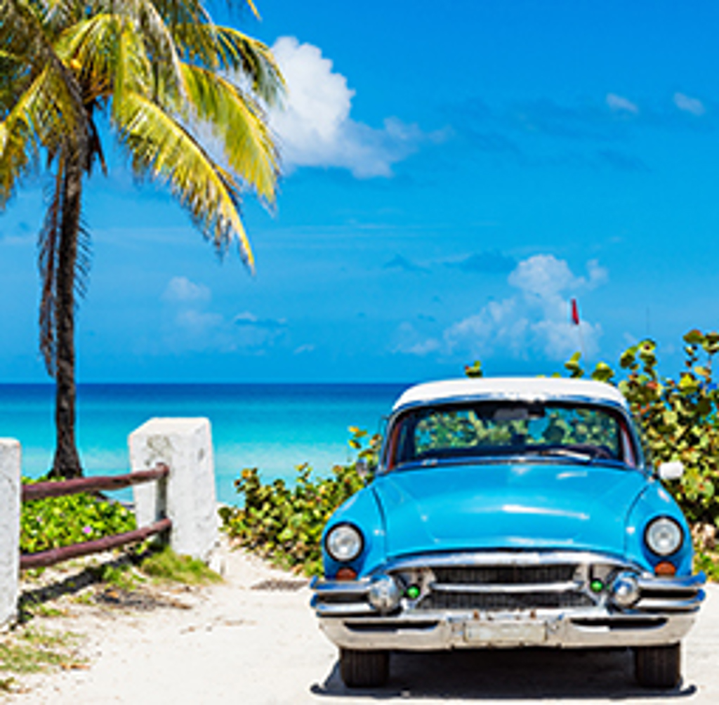 Blauwe oldtimer aan de kust met palmbomen en turkooisblauwe zee in Cuba.