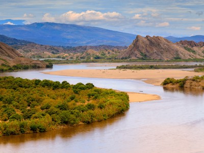 Rivierlandschap in Colombia met zandbanken, groene oevers en bergen op de achtergrond.